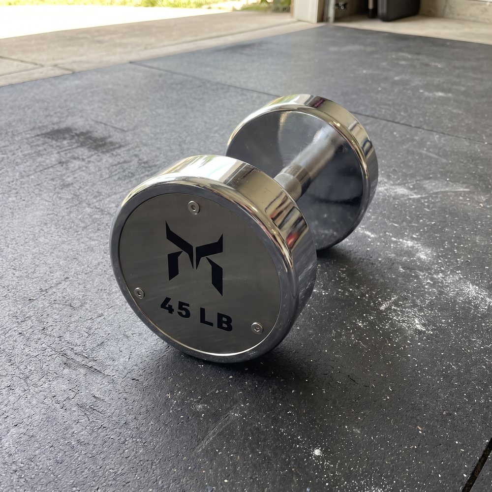 Close-up of a chrome dumbbell end cap with a black logo and 45 LB cut into brushed steel, resting on a black rubber garage mat