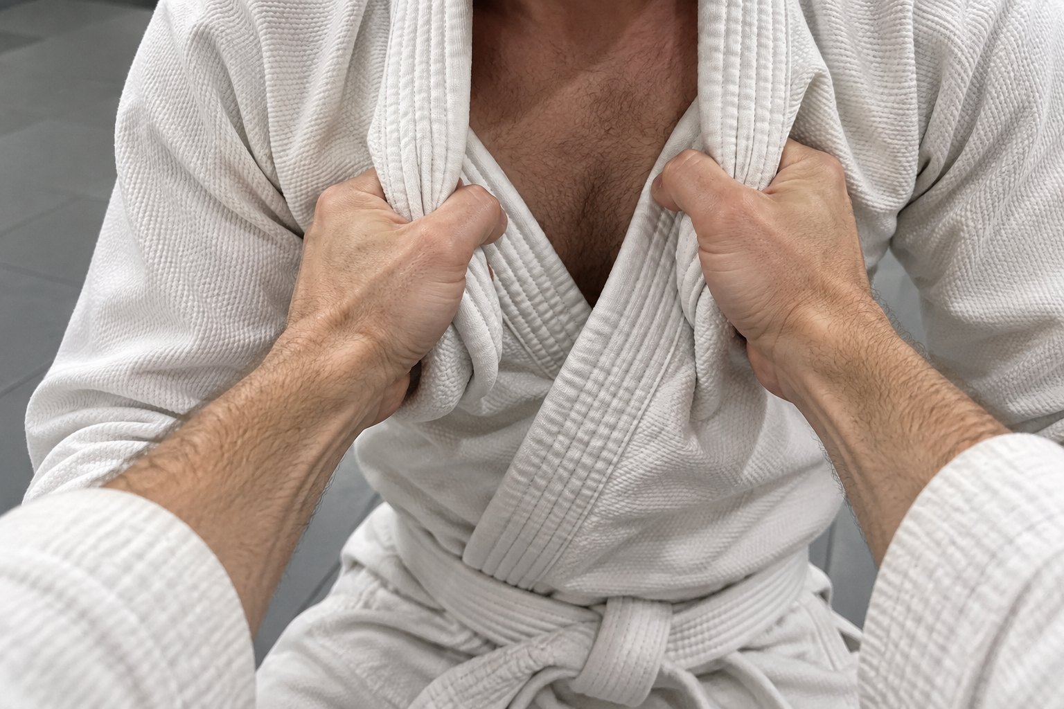 Close-up of two hands bunched deep into the thick folded collar of a white jiu-jitsu gi, fingers partly open around the cloth