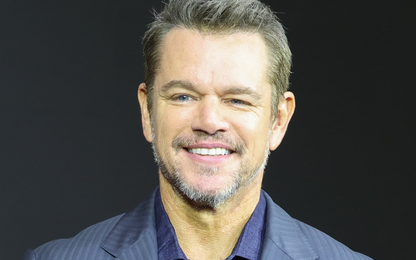 Matt Damon smiling at the press conference for The Odyssey in Seoul in August 2026, in a blue suit jacket
