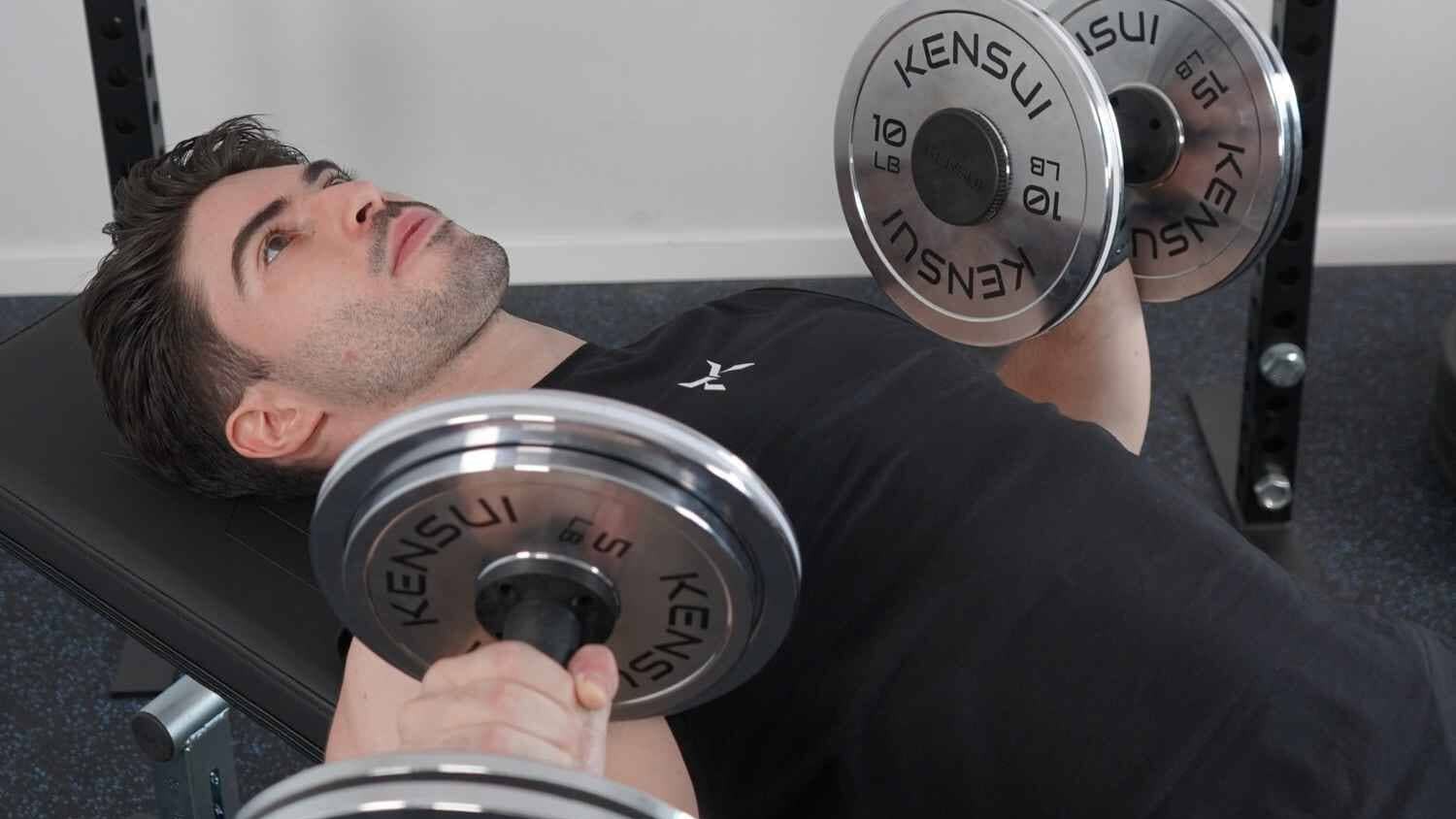 A man pressing a pair of Kensui AdaptaBELL handles loaded with chrome plates while lying on a bench