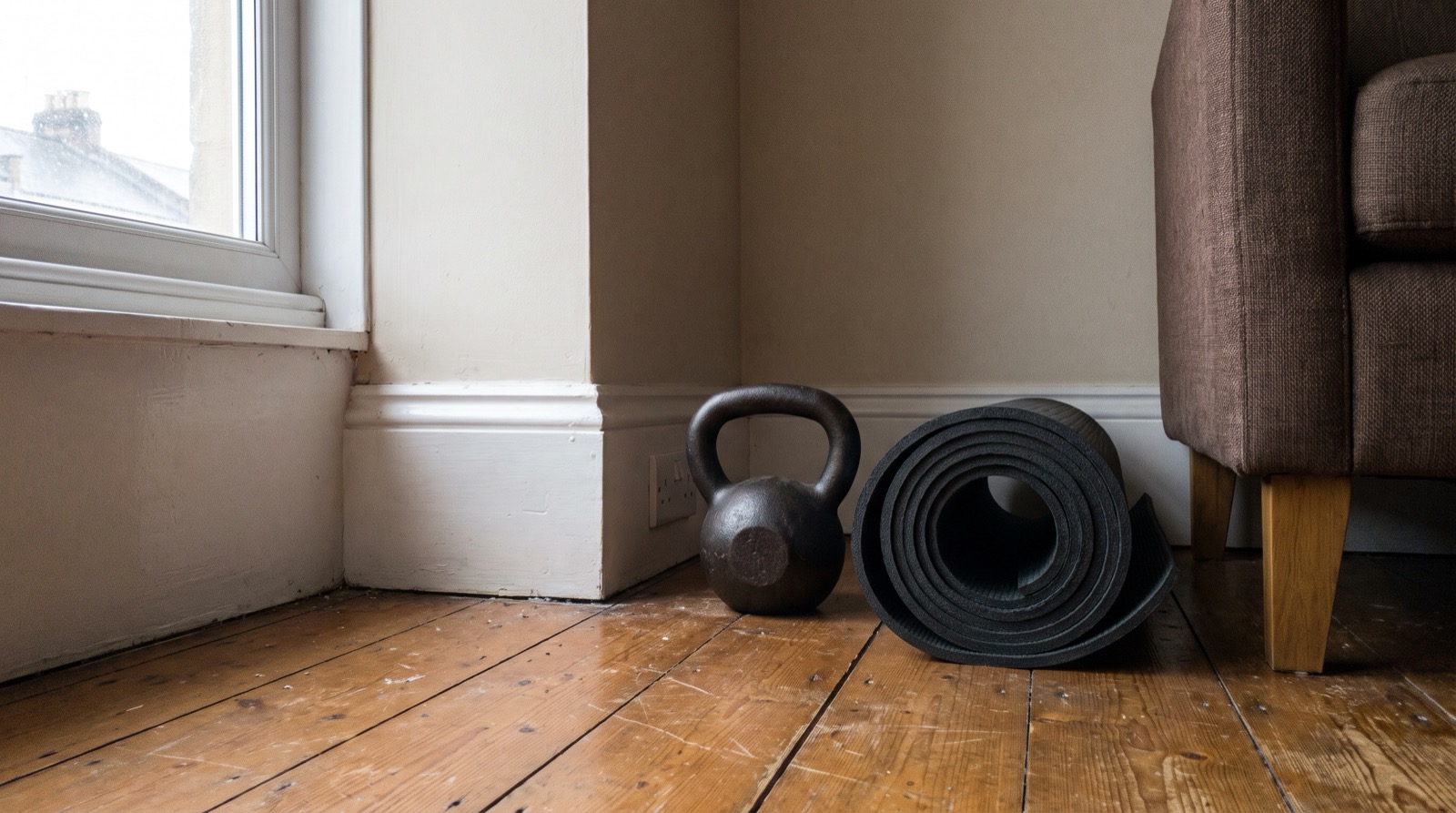 A single small cast iron kettlebell and a rolled mat in the corner of a living room