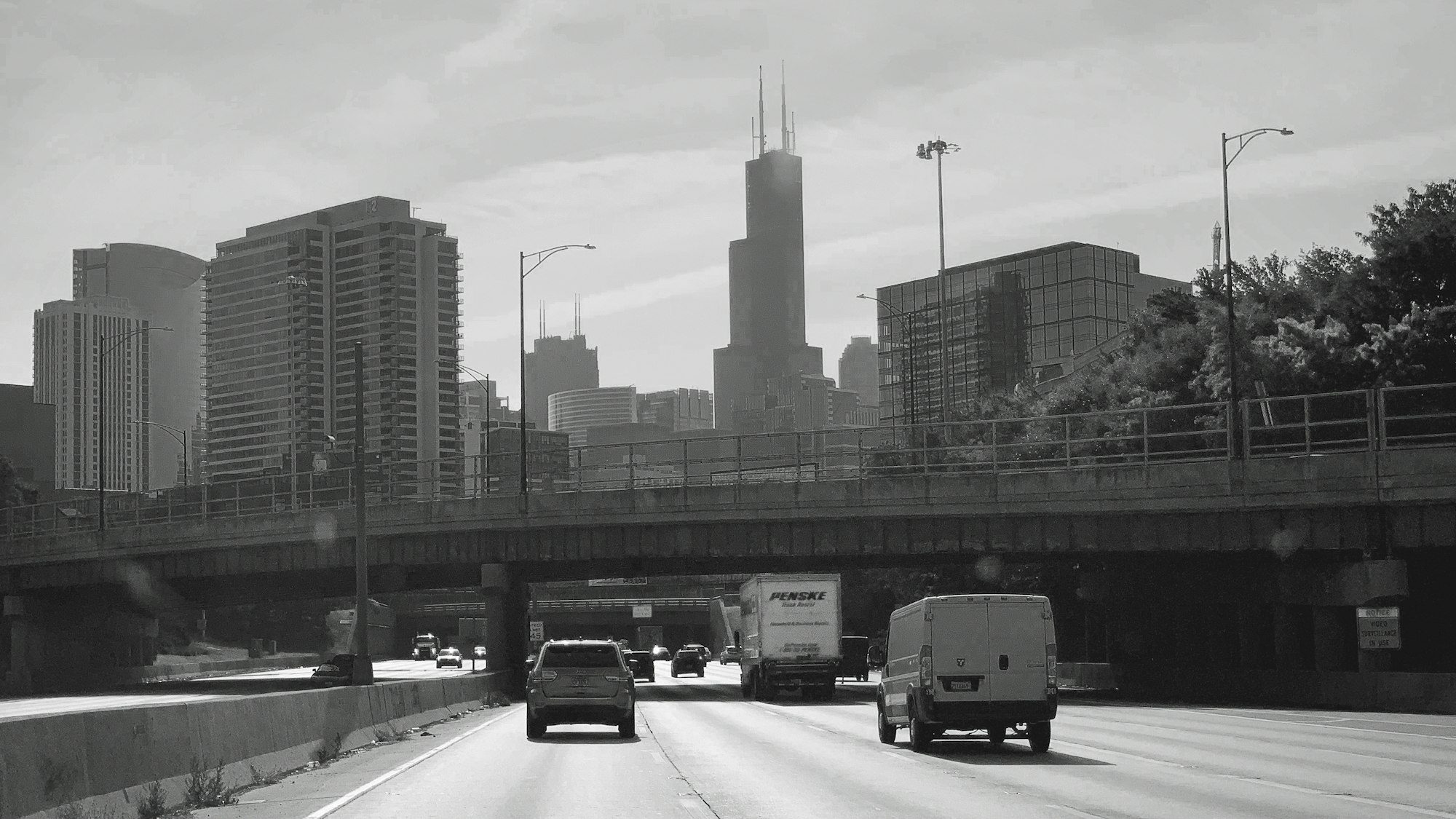 Traffic backed up on a multi-lane urban expressway beneath an overpass, city towers behind