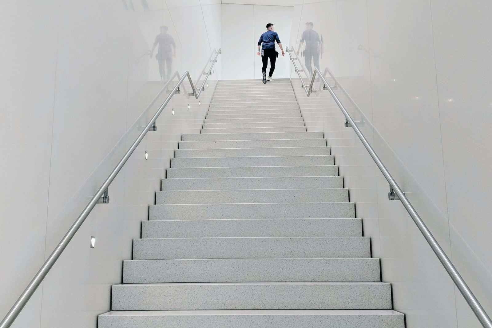 A person walking up a long, brightly lit concrete staircase