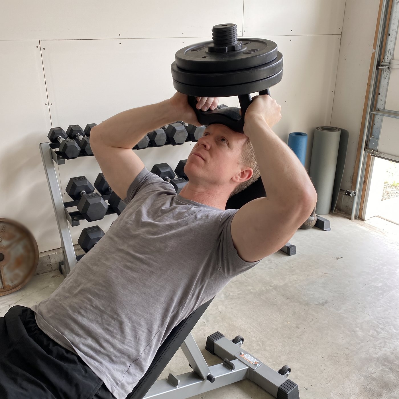 A man lying back on an incline bench holding a padded neck trainer loaded with plates against his forehead