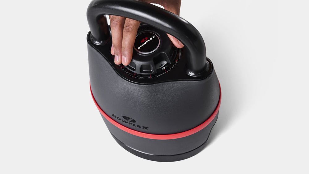 A hand turning the numbered weight-selection dial on the top of a sealed adjustable kettlebell