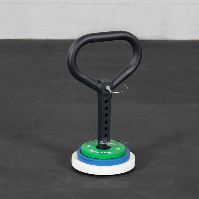 A plate-loaded kettlebell swing post standing on a gym floor with weight plates stacked at its base, below the handle
