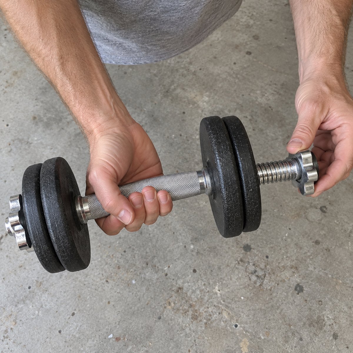 Close-up of hands on a garage floor holding a chrome spin-lock dumbbell bar whose collar has backed off, leaving a gap between the collar and the plates