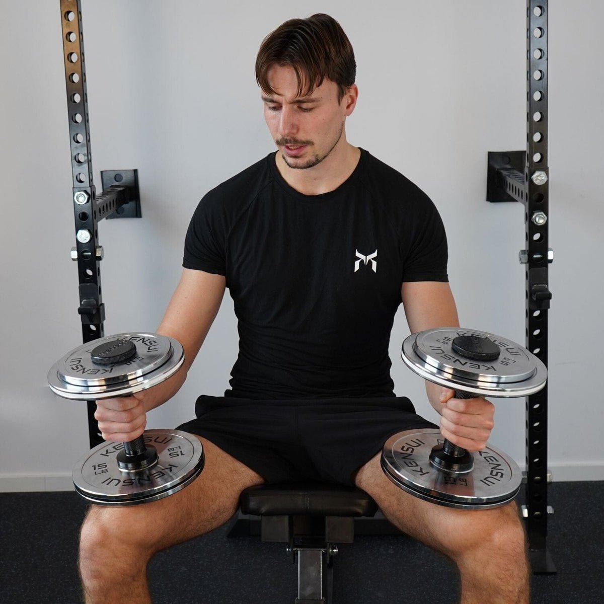 A lifter seated on a bench holding a pair of loaded Kensui AdaptaBELL handles