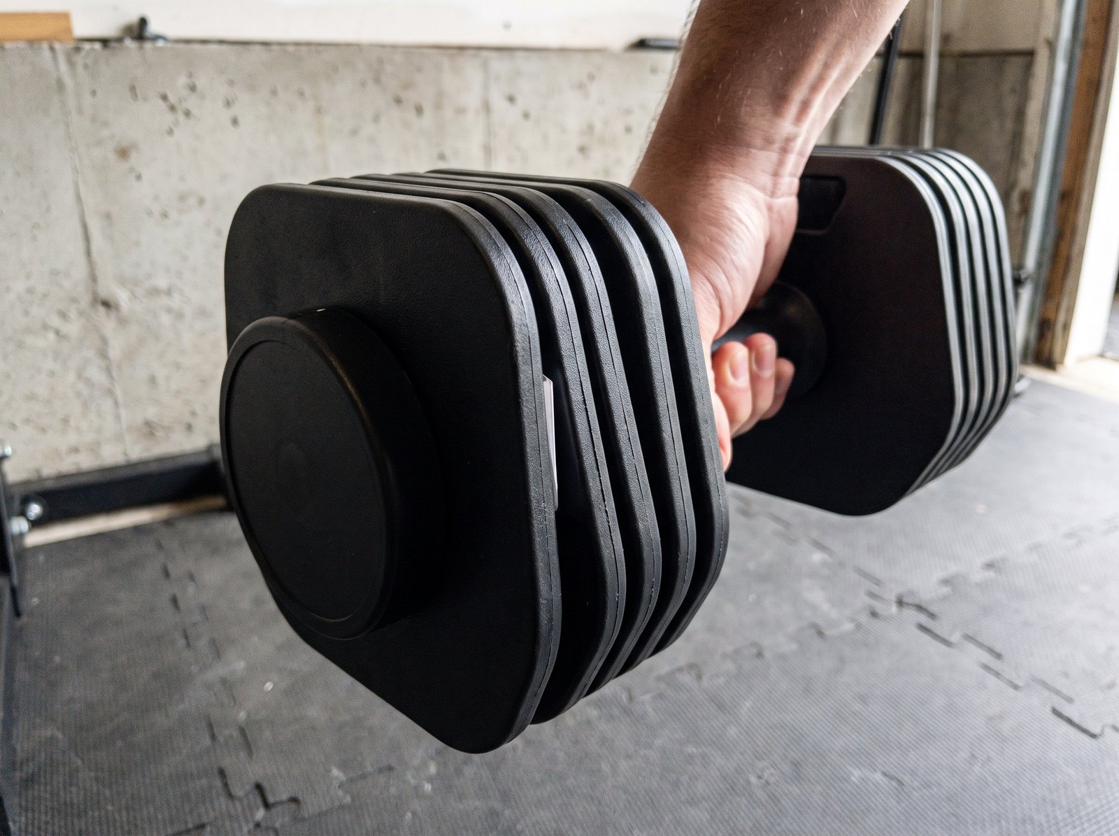 An adjustable dumbbell held in mid air with the moulded plates sitting slightly out of line and daylight showing in the gaps between them