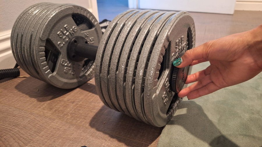 An owner's photograph of a hand holding an AdaptaBELL handle loaded with a deep stack of cast iron plates