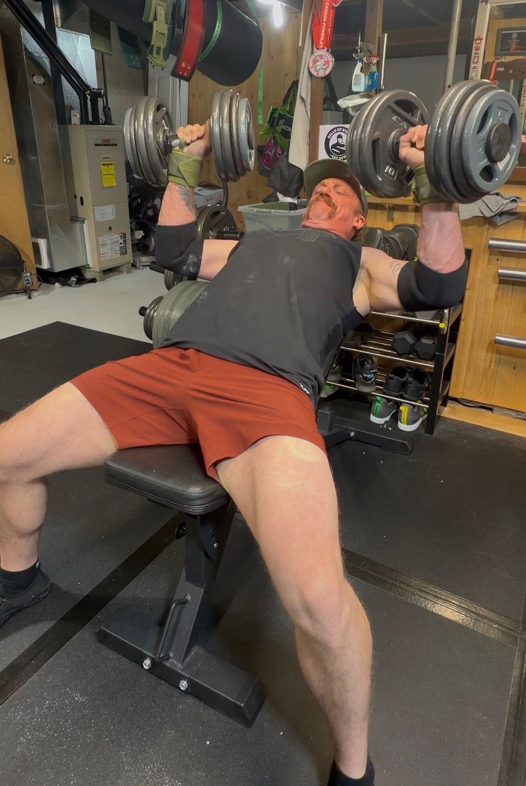 An owner in a basement gym pressing two AdaptaBELL handles loaded with Olympic plates on an incline bench