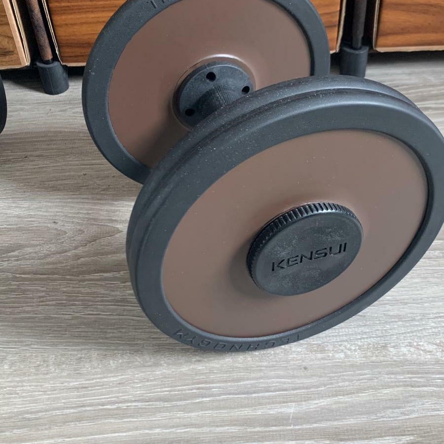 An owner's dumbbell handle standing on a wooden floor at home, loaded with brown and black plates