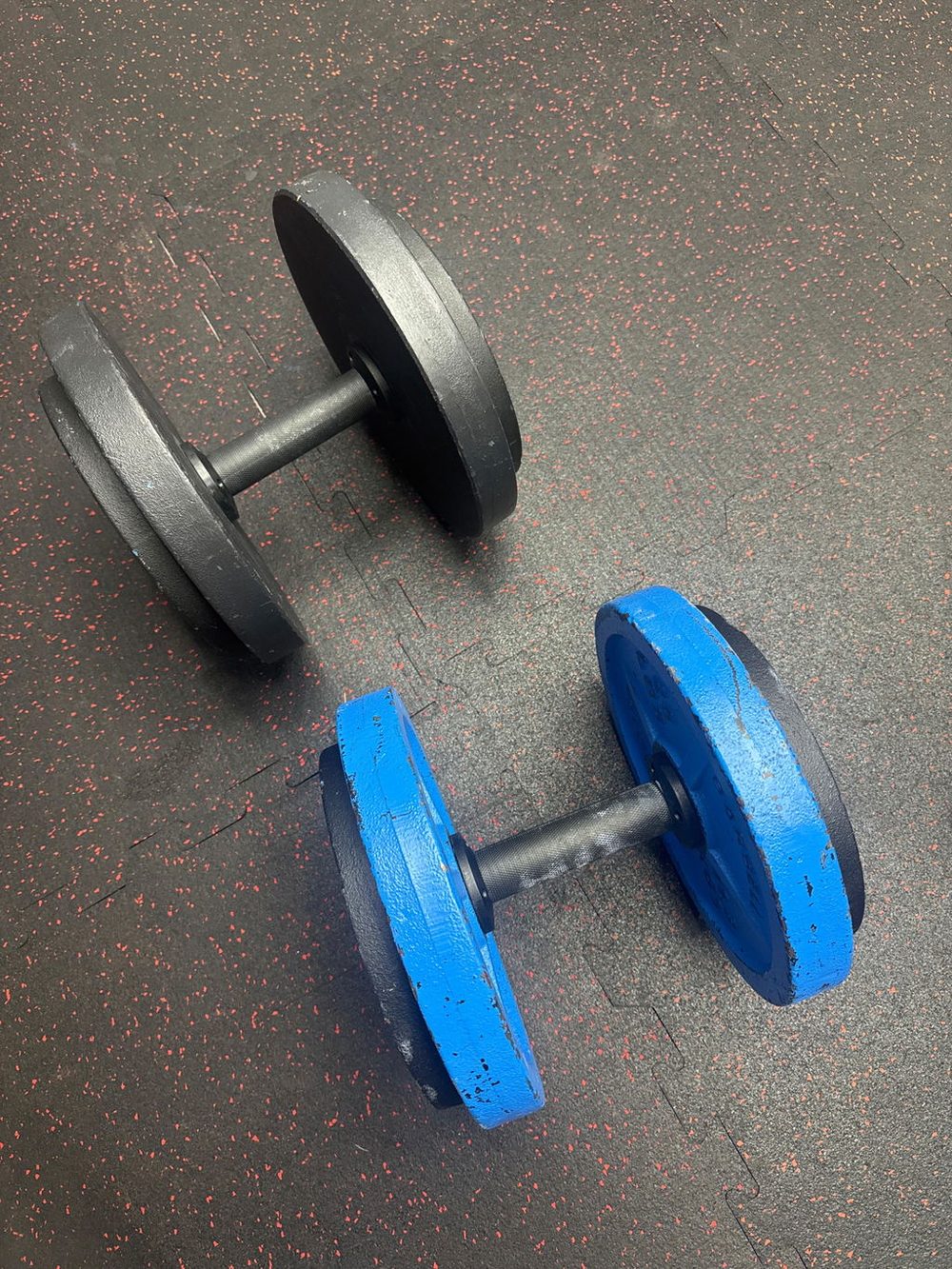 Two AdaptaBELL handles on a rubber gym floor, one loaded with black plates and one with blue plates