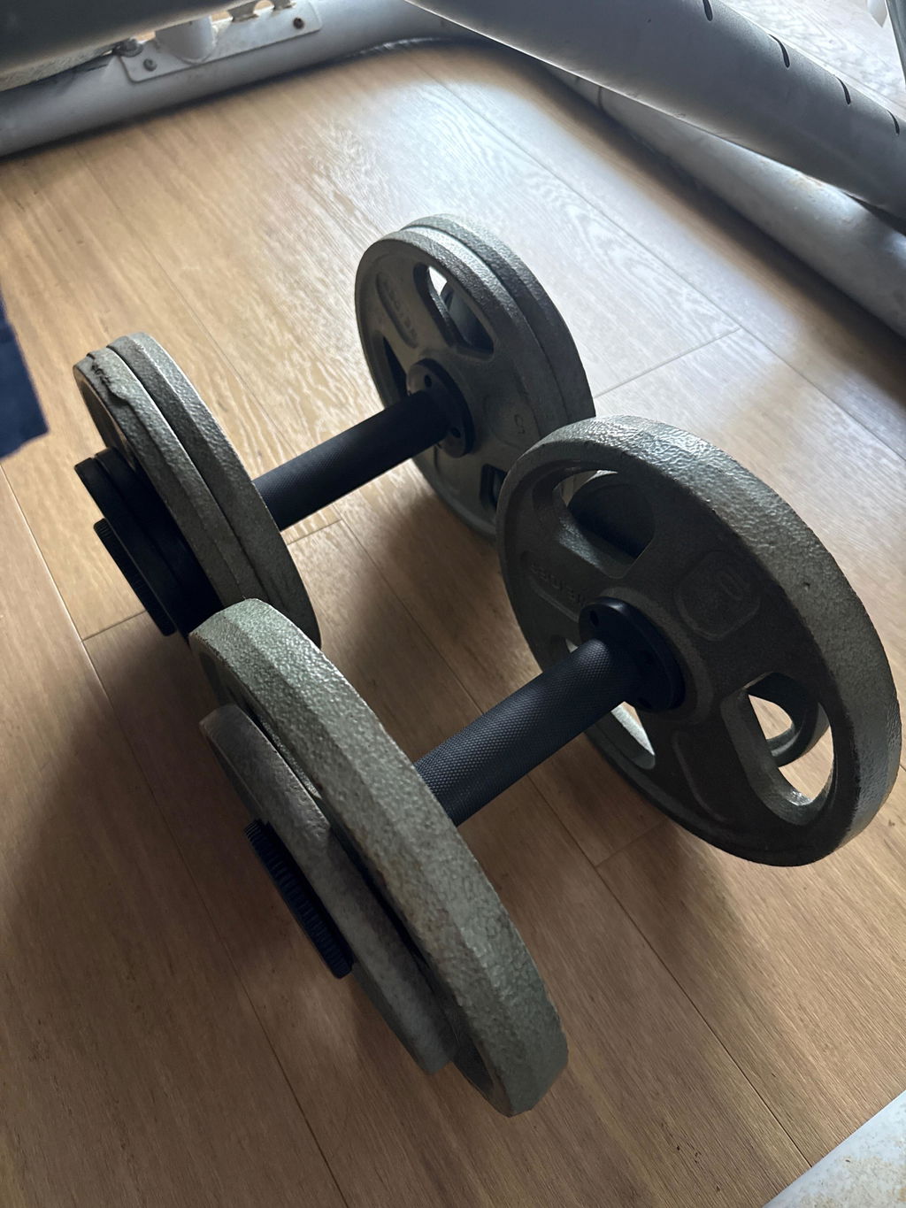 A pair of AdaptaBELL handles loaded with grey cast iron plates lying on a wooden floor