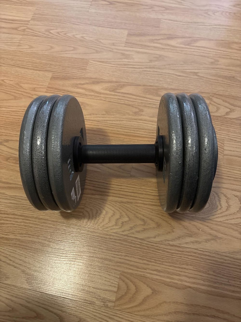 An AdaptaBELL handle loaded with three 10-pound standard plates on each side, resting on a wooden floor