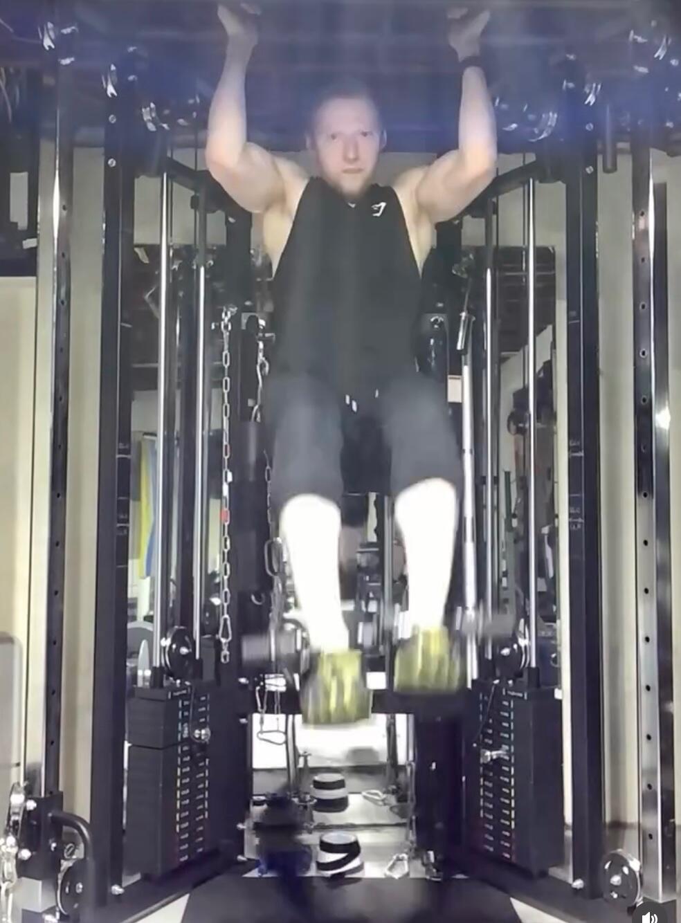 A man doing hanging leg raises at a cable station with an EZ-BOOT loaded with a plate on each foot