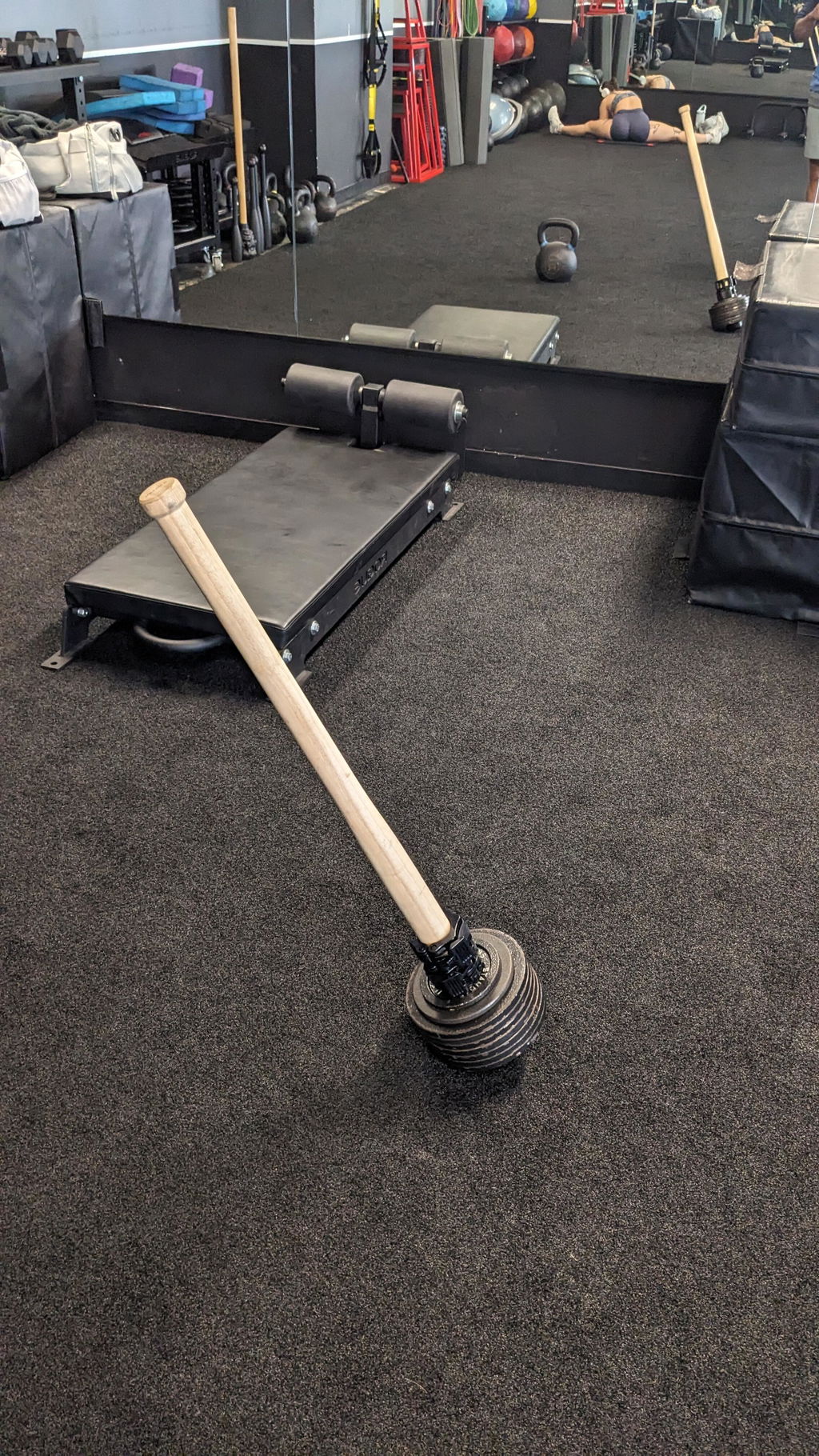 A wooden EZ-MACE with a stack of small plates on its head lying on a gym floor