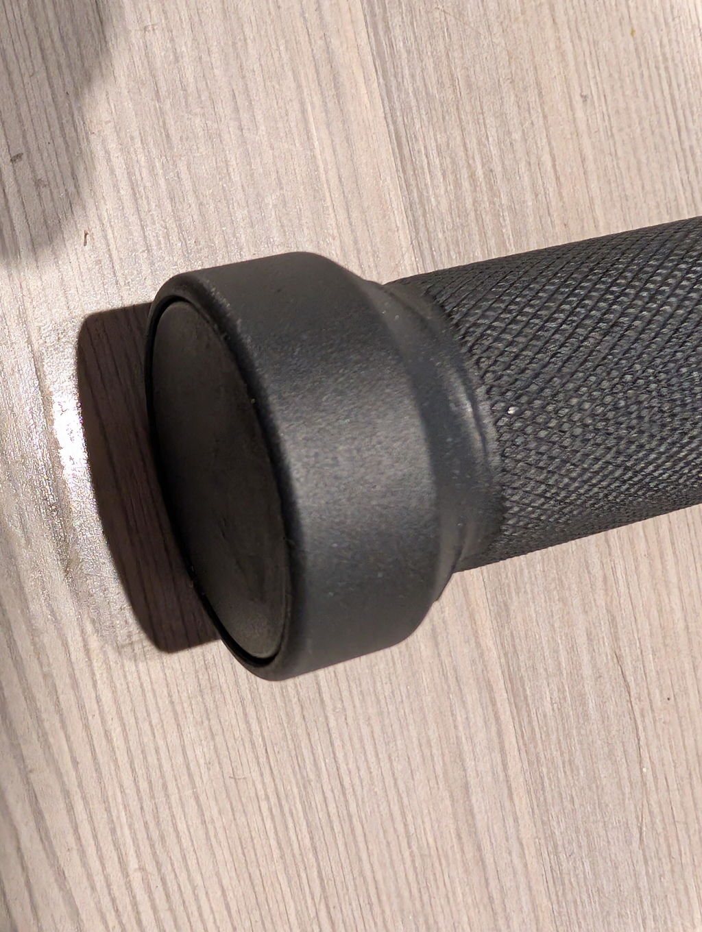 Close-up of the knurled black steel grip and end cap of an owner's steel mace on a wooden floor