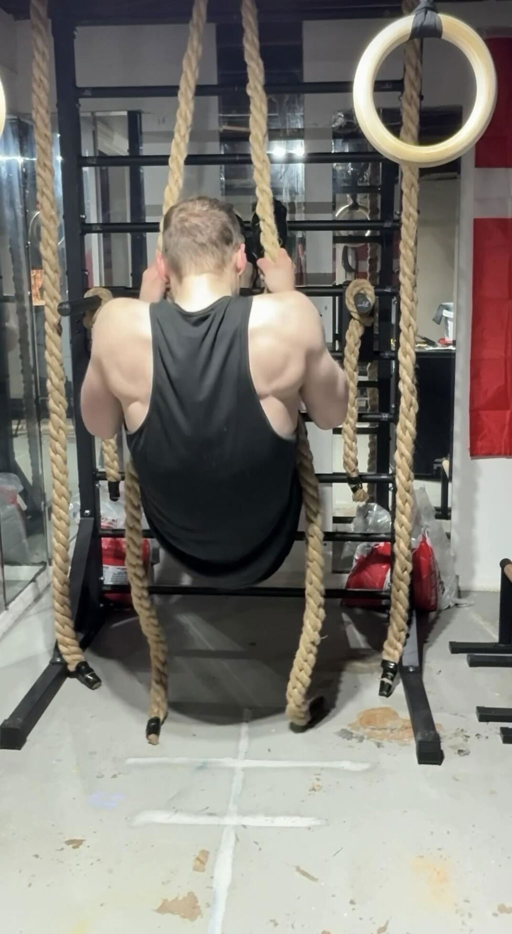 An owner seen from behind doing a pull-up on two climbing ropes in a garage gym