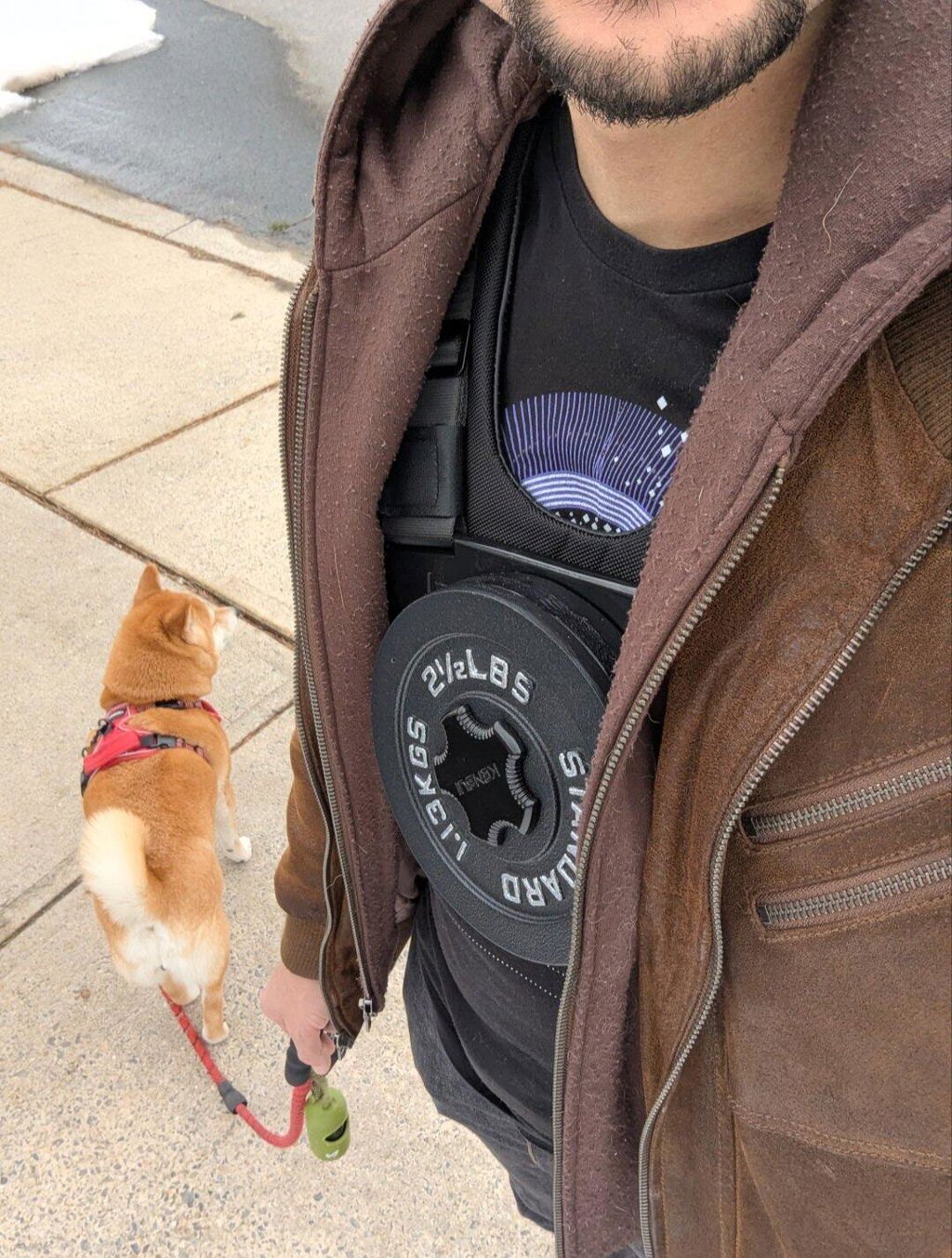 A man walking his dog on a sidewalk wearing an EZ-VEST with a plate on the chest under an open jacket