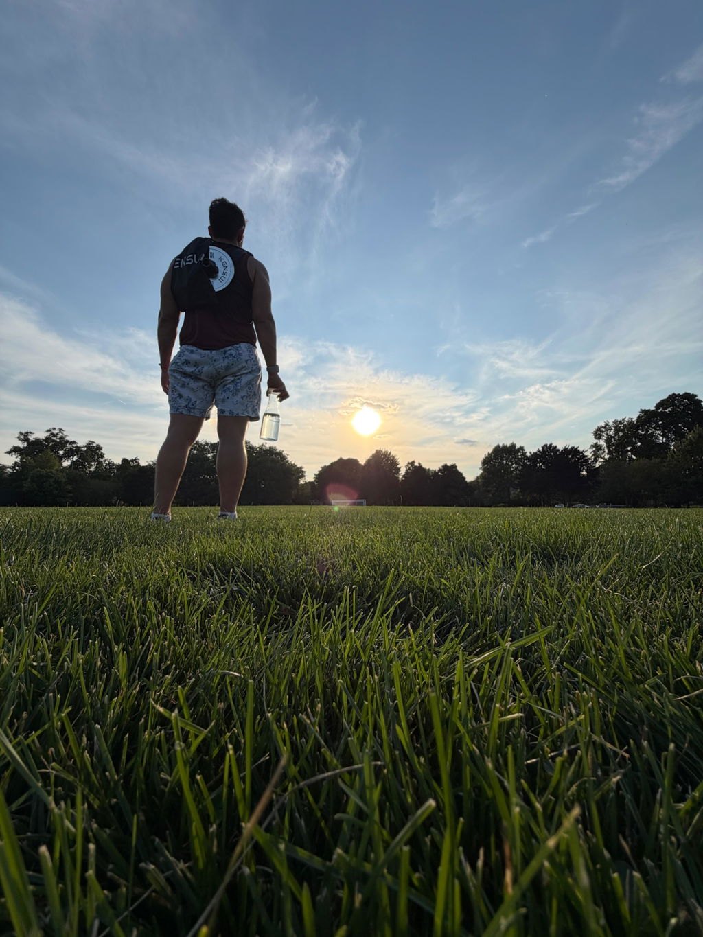 A person walking across a grassy field at sunset wearing a weight vest with a plate on the back