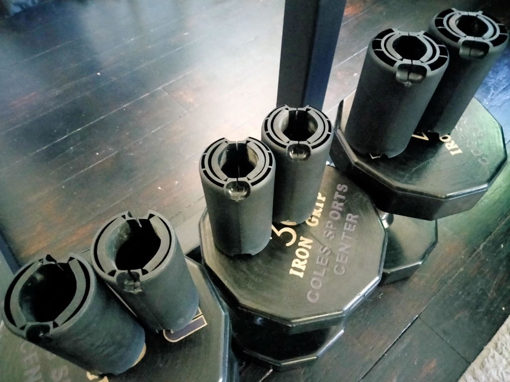 An owner's three pairs of black thick grips in three sizes, standing upright on stacked weight plates in a home gym