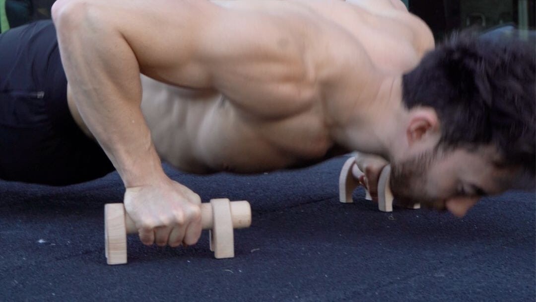 A man at the bottom of a push-up on a pair of Kensui YinYang wooden parallettes on a rubber gym mat