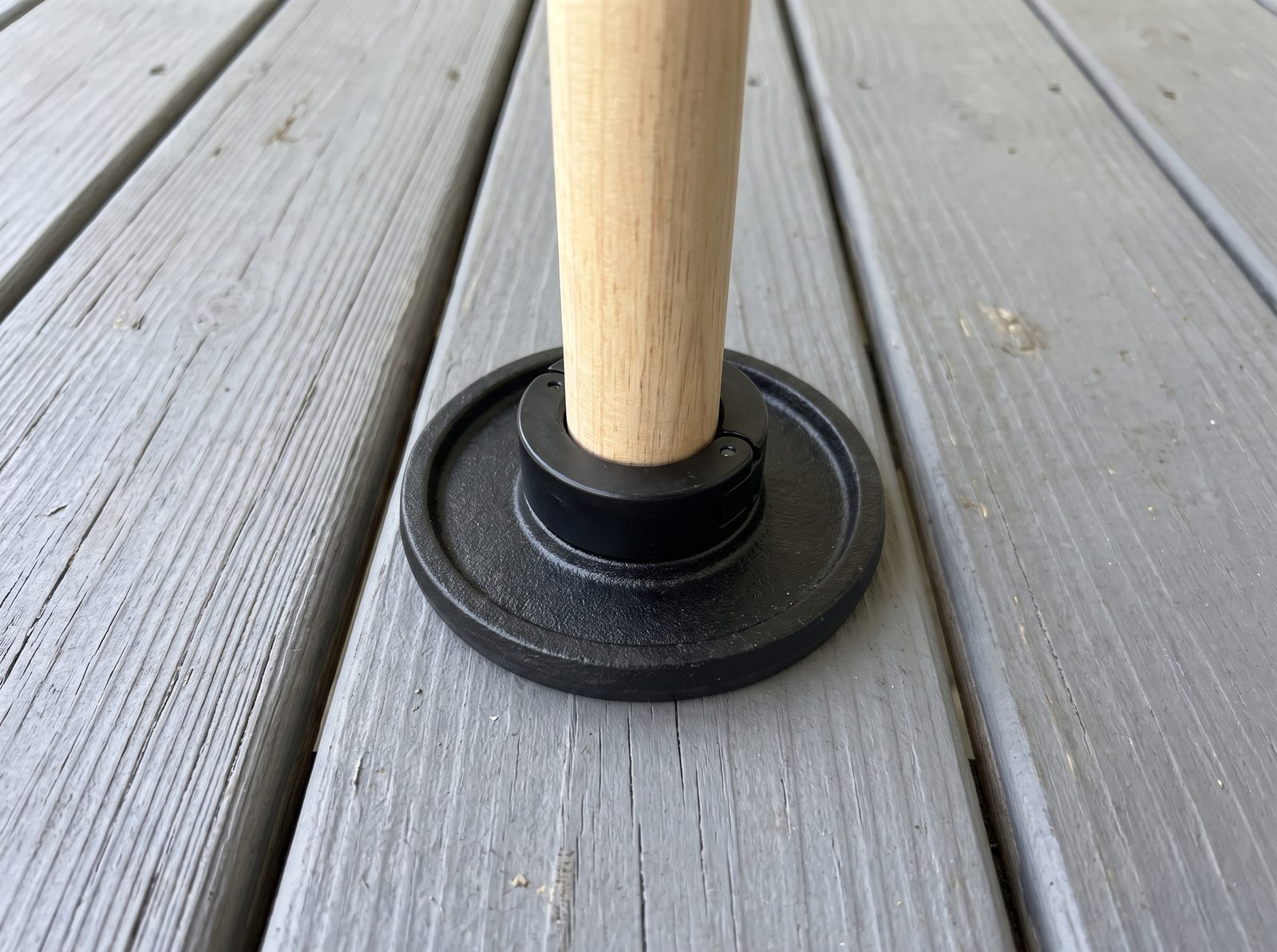 The wooden club standing on a small black plate on porch boards, its black collar seated flat on the plate