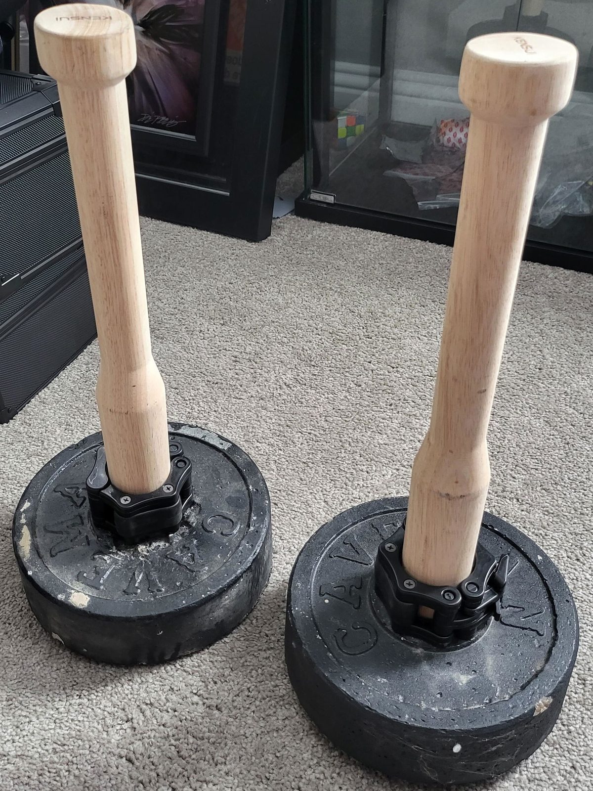 A pair of wooden plate loaded clubs standing on worn black plates on a living room carpet