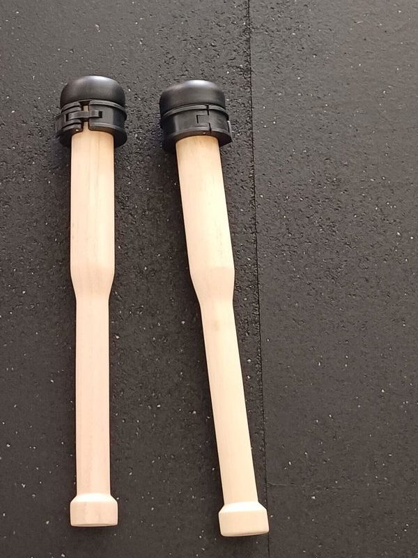 Two wooden plate loaded clubs with black collars lying side by side on a black rubber gym floor