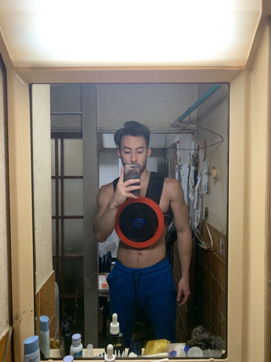 A man photographing himself in a bathroom mirror wearing an early prototype of the vest with a single red weight plate loaded on the chest