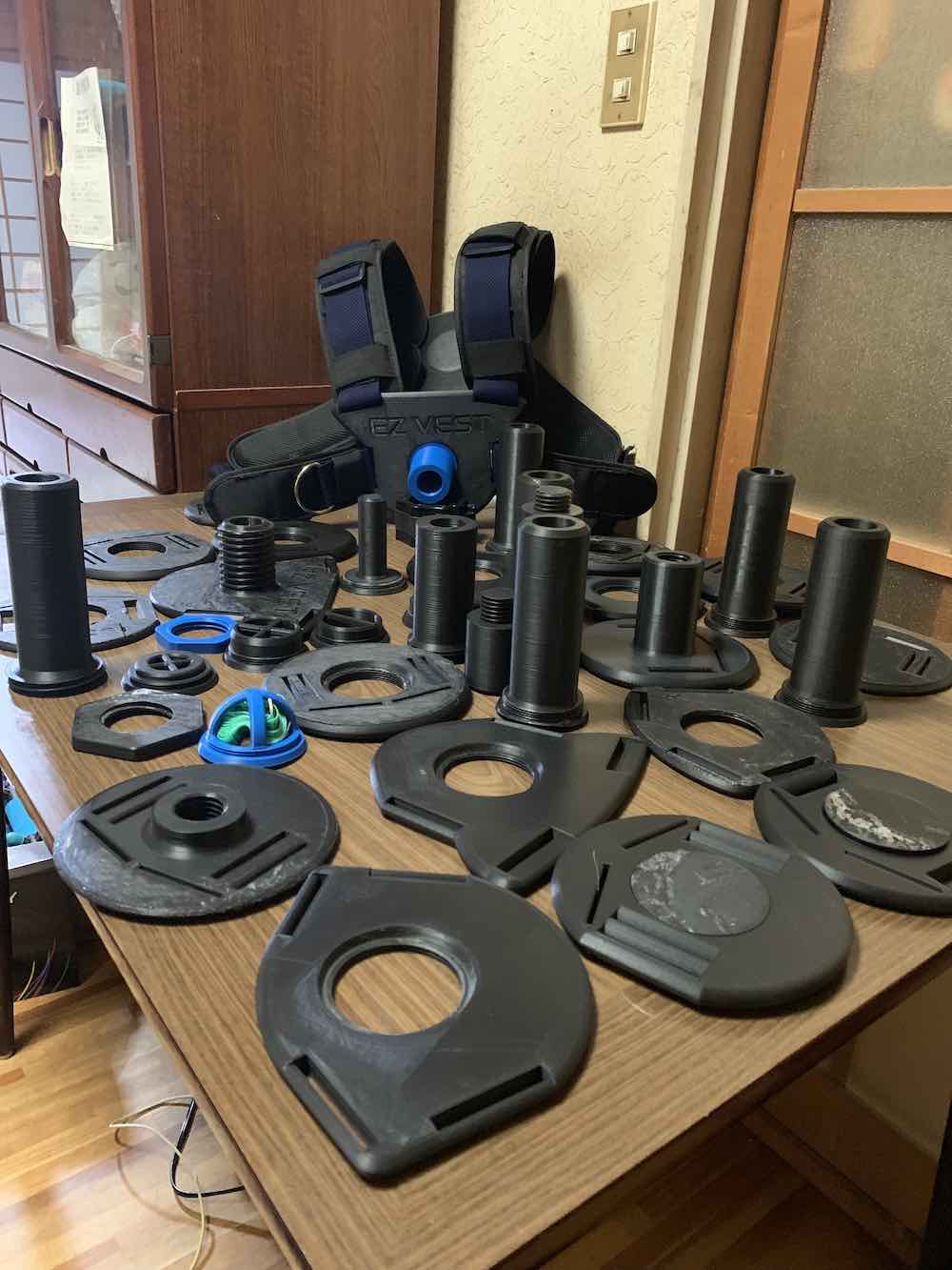 Dozens of failed 3D-printed weight vest parts, posts, collars and plate adapters spread across a dining room table