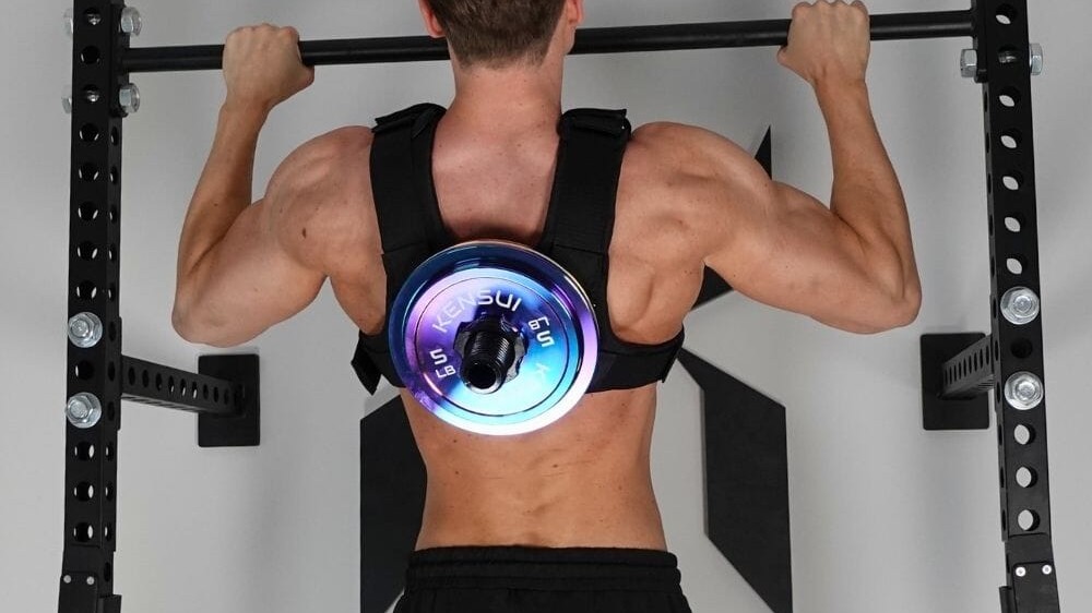 A man seen from behind doing a pull-up in a Kensui EZ-VEST loaded with a weight plate on the back