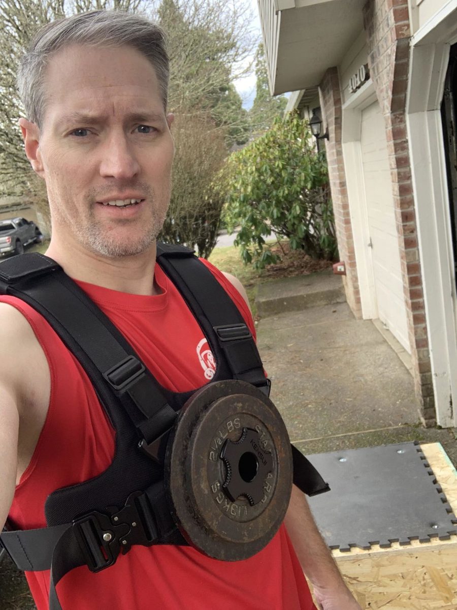 An owner in a red shirt wearing the vest with an iron plate on his chest outside his garage